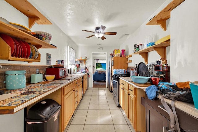 kitchen featuring stainless steel gas range, light tile patterned floors, and ceiling fan