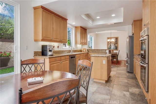 kitchen with an inviting chandelier, appliances with stainless steel finishes, a raised ceiling, light stone countertops, and pendant lighting