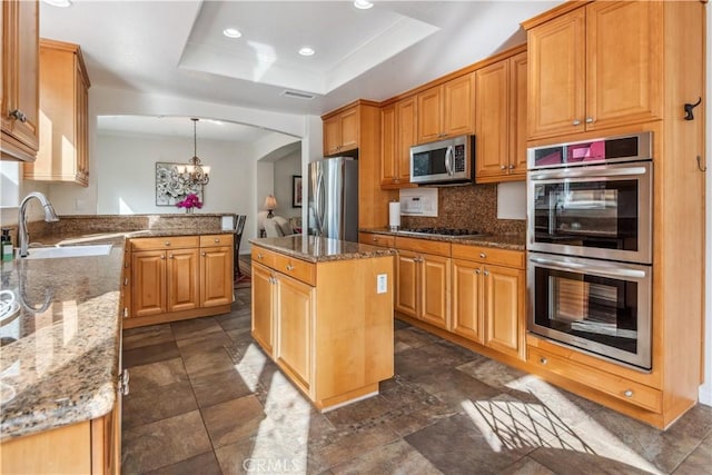 kitchen with a center island, stainless steel appliances, hanging light fixtures, a raised ceiling, and a notable chandelier