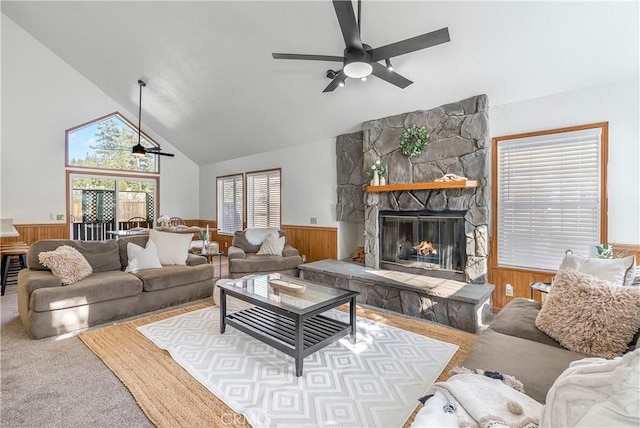 living room featuring ceiling fan, carpet floors, a stone fireplace, and wooden walls