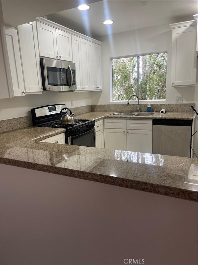 kitchen with stainless steel appliances, sink, white cabinets, and dark stone counters