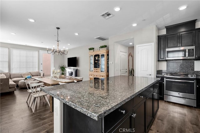 kitchen with a kitchen island, dark hardwood / wood-style flooring, stainless steel appliances, dark stone countertops, and a chandelier