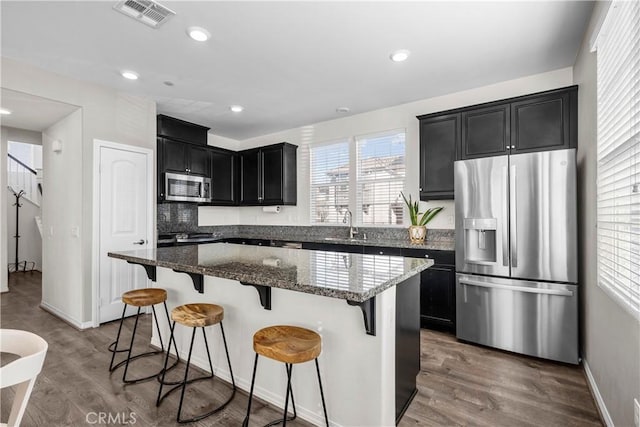 kitchen with a breakfast bar area, stainless steel appliances, dark hardwood / wood-style floors, dark stone counters, and a kitchen island