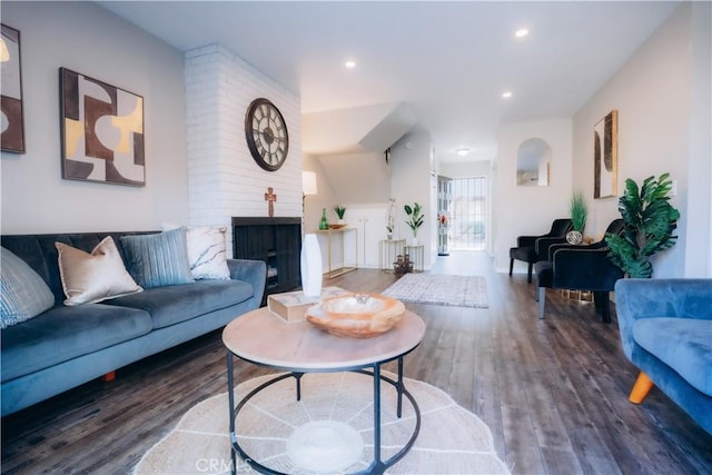 living room featuring a brick fireplace and dark wood-type flooring