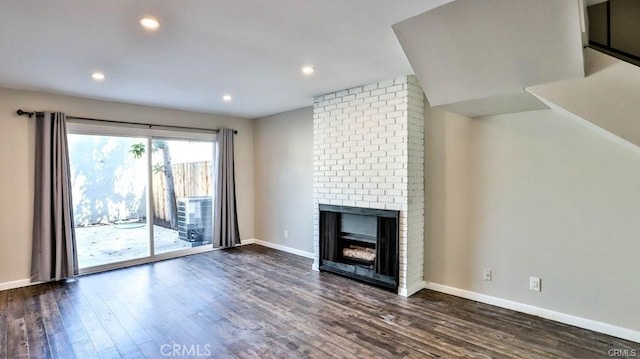 unfurnished living room with a brick fireplace and dark wood-type flooring