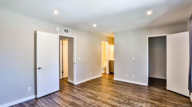 unfurnished bedroom with a walk in closet, ensuite bathroom, and dark hardwood / wood-style floors