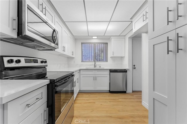 kitchen featuring light hardwood / wood-style floors, sink, white cabinetry, a paneled ceiling, and appliances with stainless steel finishes