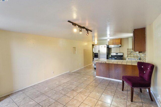 kitchen with sink, tile counters, light tile patterned floors, kitchen peninsula, and stainless steel appliances