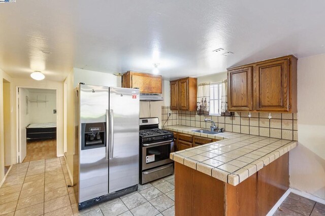 kitchen featuring sink, stainless steel appliances, tasteful backsplash, tile countertops, and kitchen peninsula