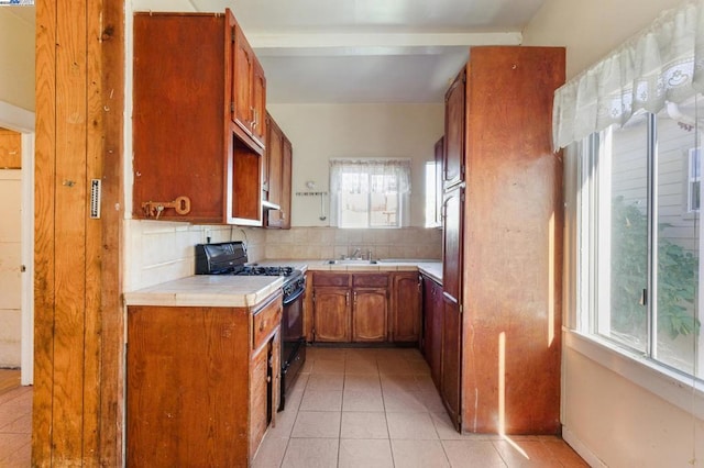 kitchen with sink, black gas range, tasteful backsplash, a wealth of natural light, and light tile patterned flooring