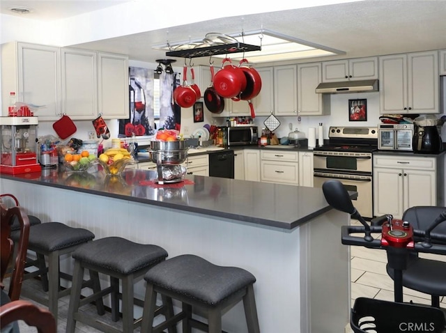 kitchen with kitchen peninsula, appliances with stainless steel finishes, light tile patterned flooring, and a kitchen bar