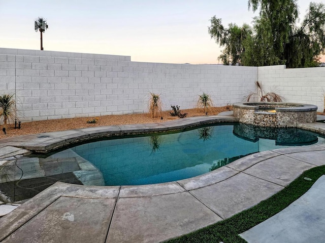 pool at dusk featuring an in ground hot tub