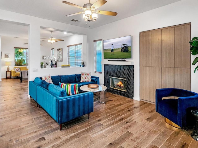 living room with ceiling fan, plenty of natural light, wood-type flooring, and a tile fireplace