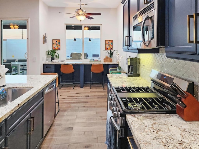 kitchen with light wood-type flooring, appliances with stainless steel finishes, a healthy amount of sunlight, and decorative backsplash