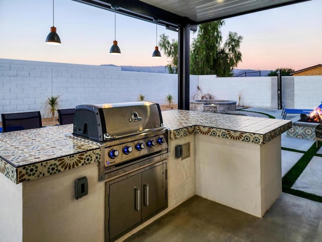 patio terrace at dusk with an outdoor kitchen, an outdoor fire pit, and area for grilling