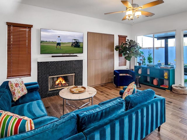 living room with ceiling fan, wood-type flooring, and a tiled fireplace