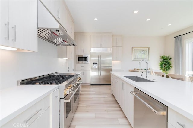 kitchen with built in appliances, sink, white cabinets, and light wood-type flooring