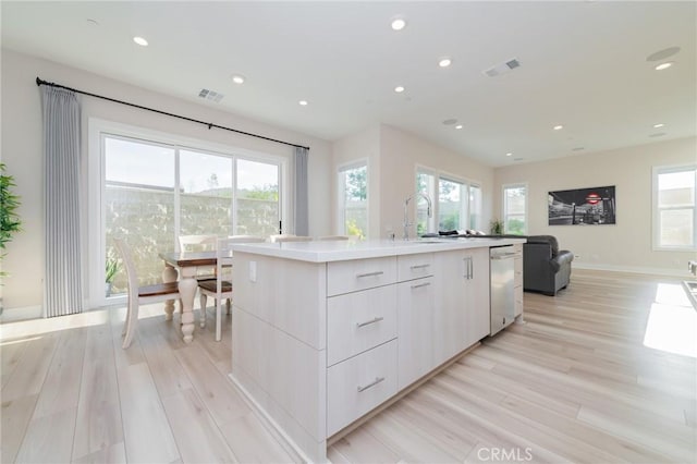 kitchen featuring white cabinetry, stainless steel dishwasher, an island with sink, and light wood-type flooring