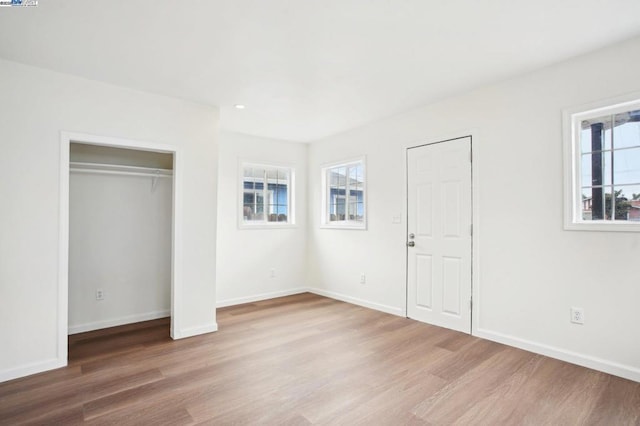 unfurnished bedroom featuring multiple windows, hardwood / wood-style floors, and a closet