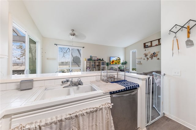 kitchen with ceiling fan, a sink, vaulted ceiling, stainless steel dishwasher, and tile counters