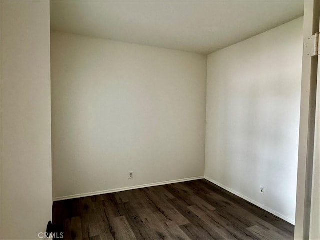 empty room featuring baseboards and dark wood-type flooring