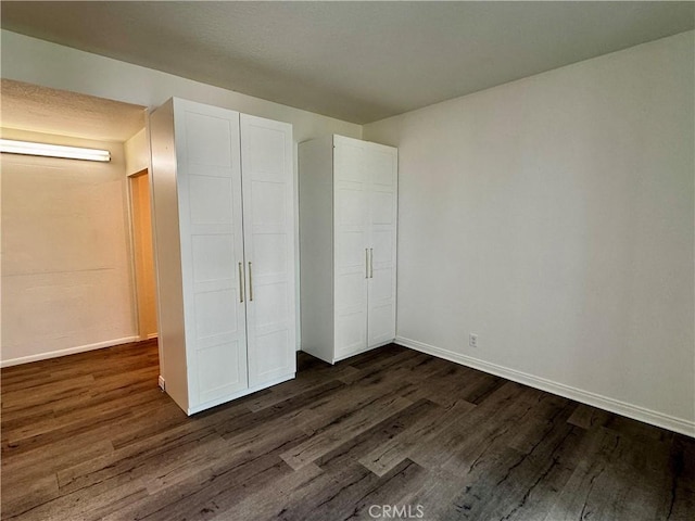 unfurnished bedroom with dark wood-style floors, a closet, and baseboards