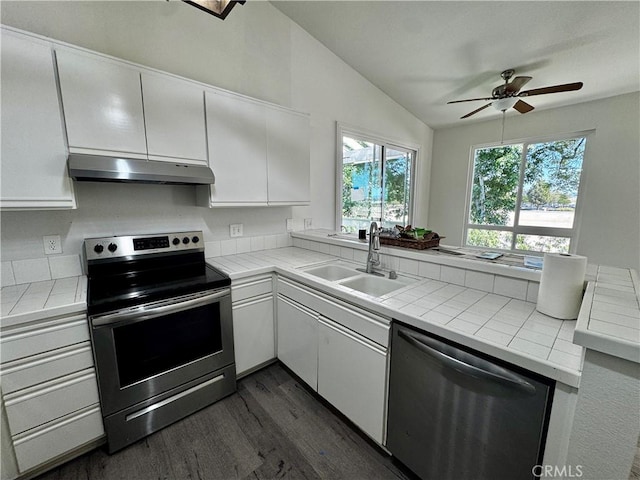 kitchen featuring tile counters, appliances with stainless steel finishes, under cabinet range hood, white cabinetry, and a sink