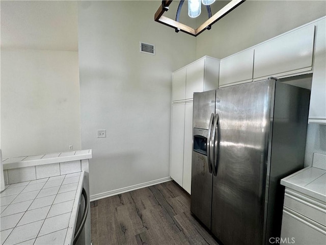 kitchen featuring visible vents, baseboards, tile counters, dark wood-style floors, and stainless steel fridge