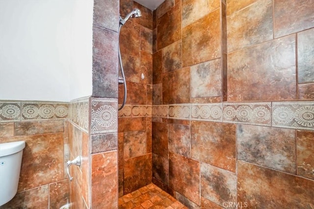 bathroom with toilet, a tile shower, and tile walls