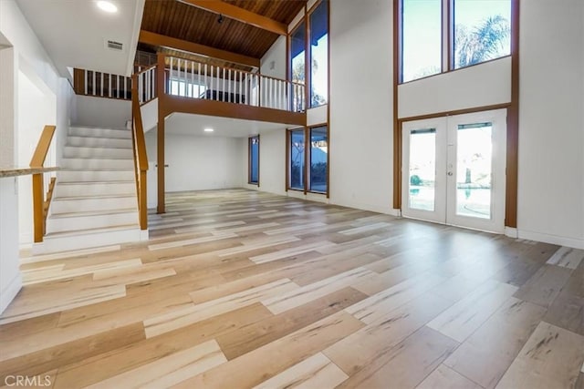 interior space featuring a towering ceiling, beamed ceiling, light hardwood / wood-style flooring, wood ceiling, and french doors