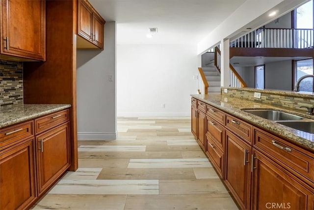 kitchen featuring light stone countertops, light hardwood / wood-style flooring, backsplash, and sink