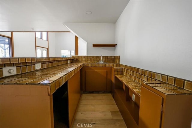 kitchen with tile counters, light hardwood / wood-style flooring, kitchen peninsula, and sink