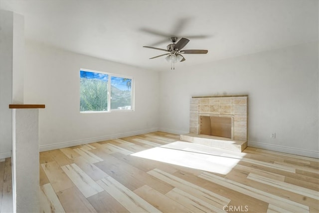 unfurnished living room featuring ceiling fan, light wood-type flooring, and a tile fireplace