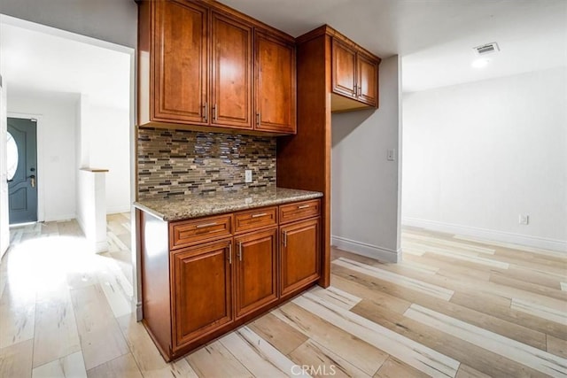 kitchen featuring tasteful backsplash, light wood-type flooring, and light stone counters