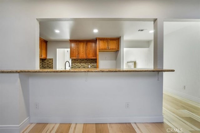 kitchen with light wood-type flooring, decorative backsplash, kitchen peninsula, and a breakfast bar