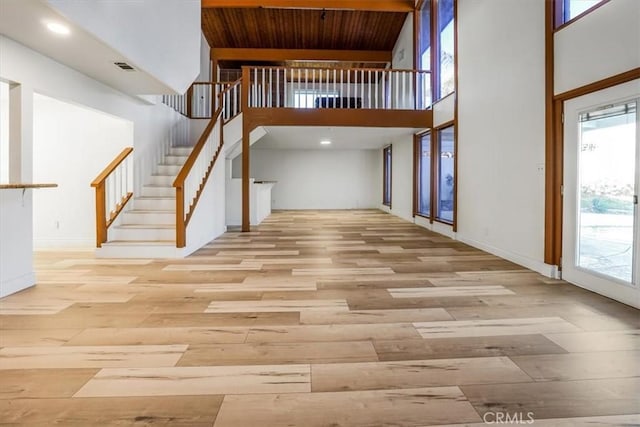 interior space with light wood-type flooring, a towering ceiling, and wooden ceiling