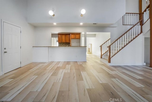 unfurnished living room featuring a high ceiling and light hardwood / wood-style flooring