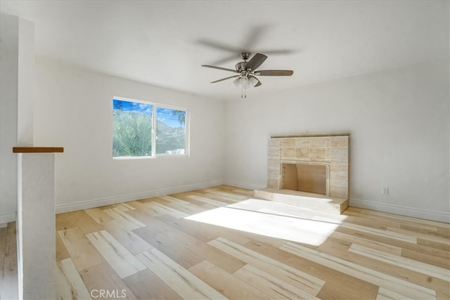 unfurnished living room with ceiling fan, a tiled fireplace, and light hardwood / wood-style flooring