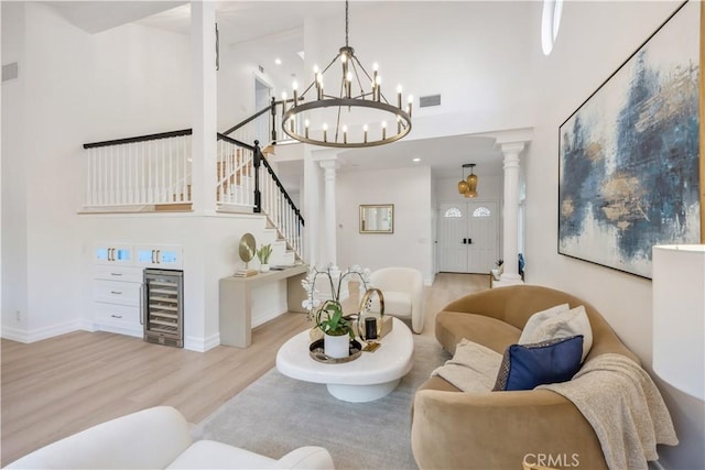 living room featuring wine cooler, light hardwood / wood-style flooring, decorative columns, and a towering ceiling