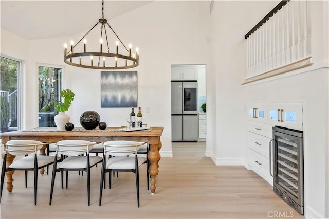 dining area featuring a notable chandelier, light hardwood / wood-style flooring, high vaulted ceiling, and beverage cooler