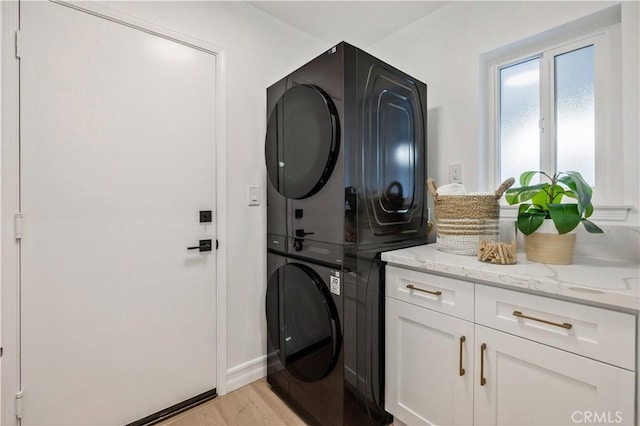 laundry room featuring cabinets, light hardwood / wood-style flooring, and stacked washer and clothes dryer