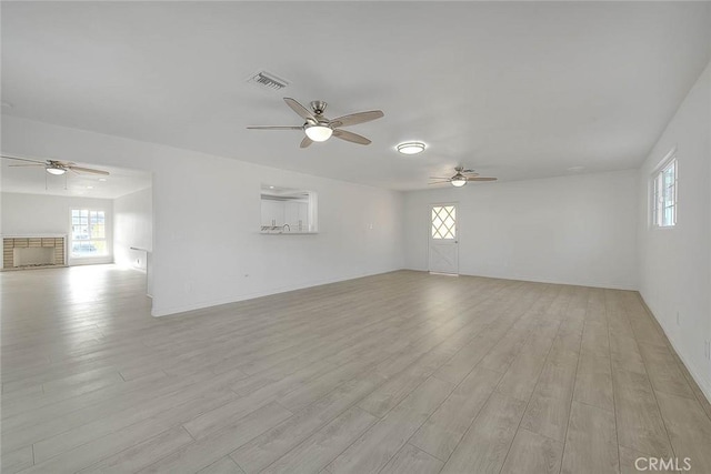 empty room with light hardwood / wood-style floors, ceiling fan, and a stone fireplace