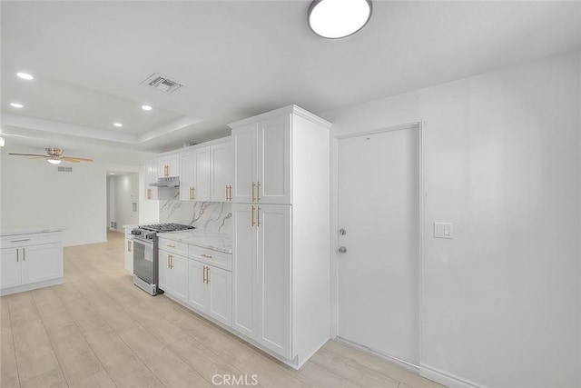 kitchen featuring ceiling fan, decorative backsplash, stainless steel range with gas cooktop, light stone countertops, and white cabinets