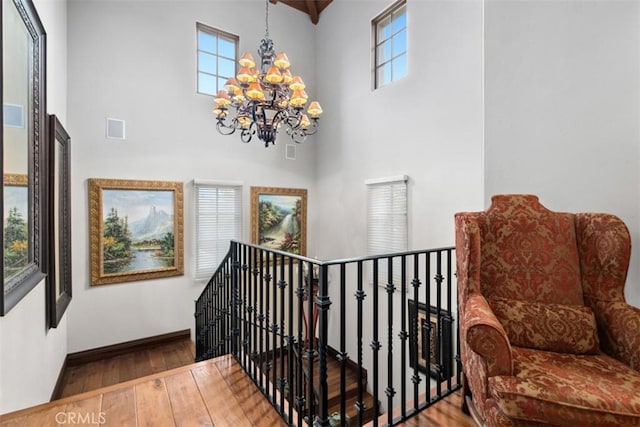 stairs with wood-type flooring, a towering ceiling, and an inviting chandelier