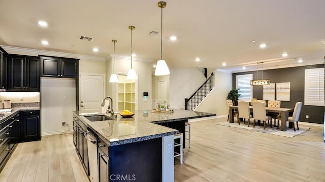 kitchen featuring a large island with sink, pendant lighting, a breakfast bar, sink, and light stone counters