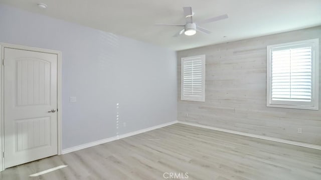 unfurnished room featuring ceiling fan, light wood-type flooring, and wooden walls