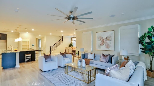 living room featuring ceiling fan, sink, ornamental molding, and light wood-type flooring