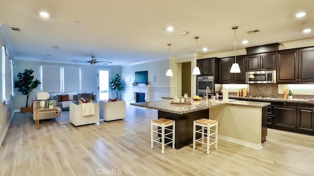 kitchen with decorative light fixtures, light hardwood / wood-style floors, a kitchen island with sink, appliances with stainless steel finishes, and a breakfast bar area