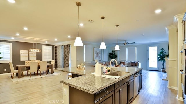 kitchen with an island with sink, ceiling fan, dark brown cabinets, hanging light fixtures, and sink