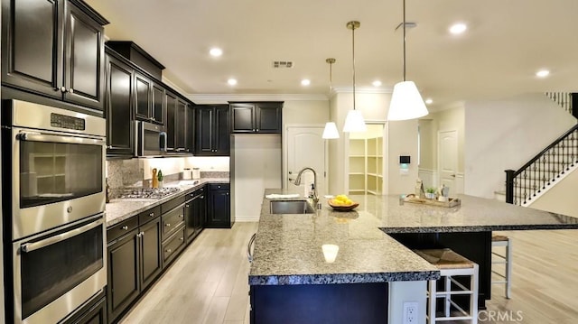 kitchen featuring light stone countertops, pendant lighting, appliances with stainless steel finishes, a spacious island, and sink